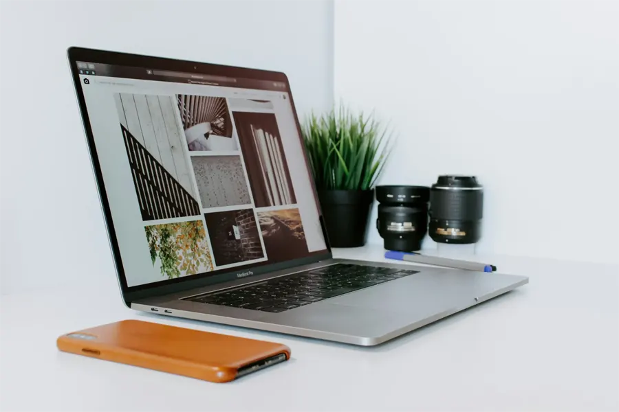 Laptop on a white desk showing a design portfolio beside camera lenses