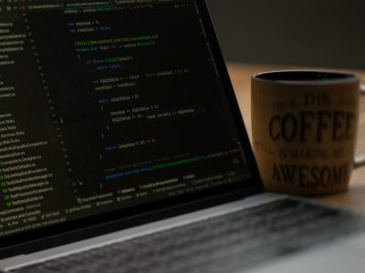 Laptop displaying code with a coffee mug featuring the phrase "THIS COFFEE IS MAKING ME AWESOME," symbolising productivity and web development for SEO-focused projects.